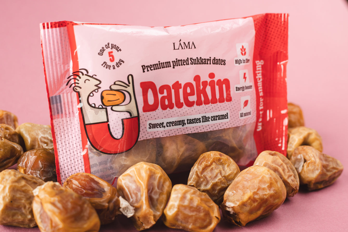 Datekin Premium Pitted Sukkari Dates are nestled among spilled dates. This nutritious snack is in striking red and white packaging with a fun cartoon character, emphasizing sweet, creamy, tastes like caramel and its one of your 5 a day. Ideal for easy shelf display and quick pick-ups.